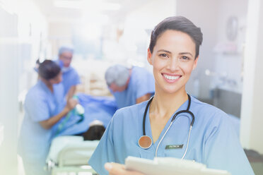 Portrait smiling, confident female surgeon with clipboard in hospital corridor - HOXF01706