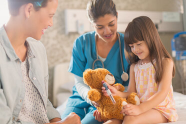 Krankenschwester und Mutter beobachten ein Mädchen, das einen Insulinstift auf einem Teddybär benutzt - HOXF01707