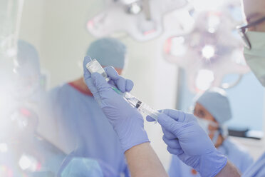 Männlicher Anästhesist mit Spritze bei der Vorbereitung von Narkosemitteln im Operationssaal - HOXF01725
