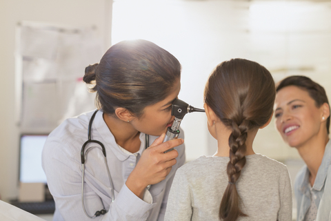 Eine Kinderärztin benutzt ein Otoskop und untersucht das Ohr eines Mädchens im Untersuchungsraum, lizenzfreies Stockfoto