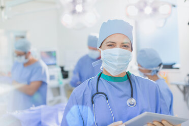 Porträt einer selbstbewussten Chirurgin mit chirurgischer Maske und digitalem Tablet im Operationssaal - HOXF01736