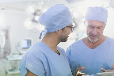 Männliche Chirurgen im Gespräch und mit digitalem Tablet im Operationssaal - HOXF01742