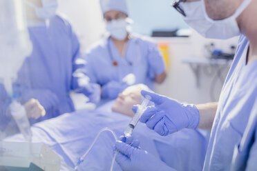 Anesthesiologist with syringe injecting anesthesia into IV drip in operating room - HOXF01747