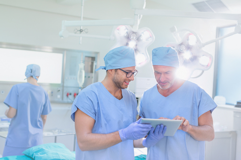 Männliche Chirurgen im Gespräch und mit digitalem Tablet im Operationssaal, lizenzfreies Stockfoto