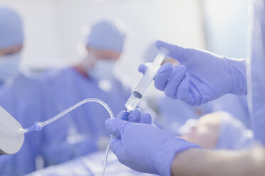 Nahaufnahme eines Anästhesisten mit einer Spritze, der Narkosemittel in einen IV-Tropf im Operationssaal injiziert - HOXF01755