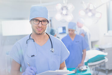 Porträt eines jungen männlichen Chirurgen mit Brille und Klemmbrett im Operationssaal - HOXF01761