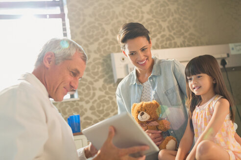 Ein männlicher Arzt zeigt einer Patientin und ihrer Mutter ein digitales Tablet im Krankenhauszimmer - HOXF01768