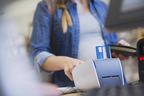 Weibliche Kundin benutzt ein Kreditkartenlesegerät in einem Geschäft - HOXF01775