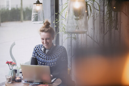 Smiling young woman using laptop in cafe window - HOXF01785