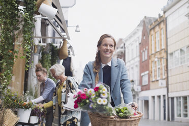 Lächelnde Frau auf dem Fahrrad mit Blumen im Korb auf einer Stadtstraße - HOXF01789