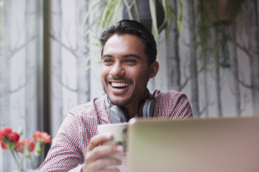 Mann lachend und Kaffee trinkend am Laptop im Café - HOXF01792