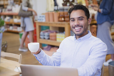 Porträt eines begeisterten jungen Mannes, der in einem Café am Laptop Kaffee trinkt - HOXF01798