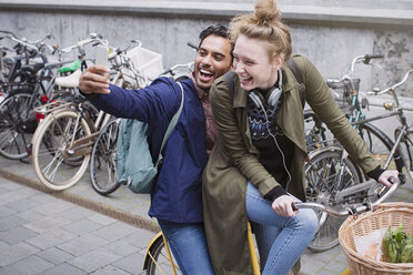 Playful, laughing young couple taking selfie with camera phone on bicycle - HOXF01805