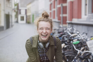 Porträt einer begeisterten, lachenden jungen Frau mit Kopfhörern auf einer Straße in der Stadt - HOXF01809