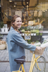 Porträt einer lächelnden Frau, die mit dem Fahrrad vor einem städtischen Laden steht - HOXF01815
