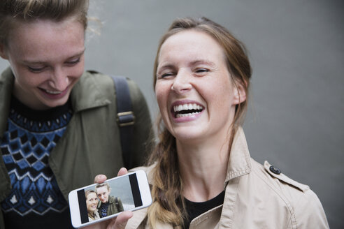 Lachende junge Frauen zeigen Selfie-Foto auf Smartphone - HOXF01823