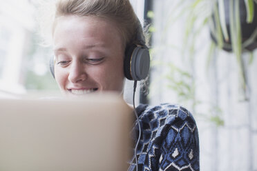 Lächelnde junge Frau mit Kopfhörern und Laptop in einem Café - HOXF01832