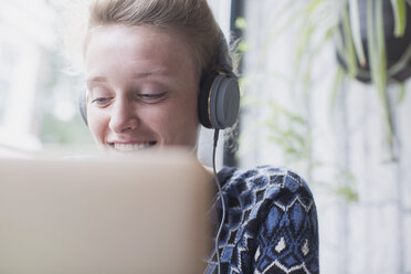 Smiling young woman with headphones using laptop in cafe - HOXF01832