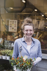 Porträt einer lächelnden Blumenhändlerin, die eine Topfpflanze im Schaufenster hält - HOXF01839