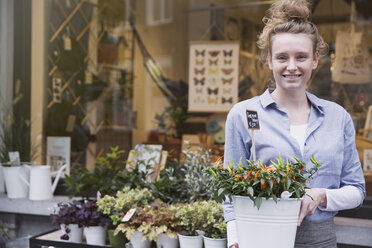 Porträt einer lächelnden Blumenhändlerin mit Topfpflanze im Schaufenster - HOXF01843