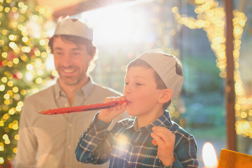 Vater und Sohn tragen Weihnachtskronen aus Papier und blasen Partygäste aus - HOXF01863