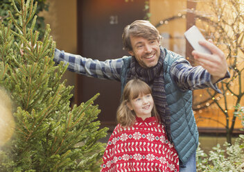 Vater und Tochter machen ein Selfie mit dem Weihnachtsbaum vor dem Haus - HOXF01864