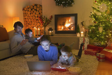 Eine Familie, die sich im weihnachtlich geschmückten Wohnzimmer mit Laptop, Tablet und Handy entspannt - HOXF01875