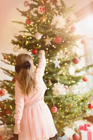 Mädchen in rosafarbenem Kleid hängt Weihnachtsschmuck an den Weihnachtsbaum, lizenzfreies Stockfoto