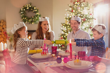 Familie mit Papierkronen zieht Weihnachtsgebäck am Esstisch - HOXF01884