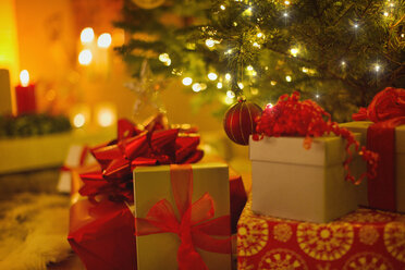 Weihnachtsgeschenke mit roten Schleifen unter dem beleuchteten Weihnachtsbaum - HOXF01888