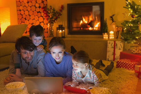 Familie isst Popcorn und sieht sich ein Video auf dem Laptop im weihnachtlichen Wohnzimmer mit Kamin an - HOXF01891