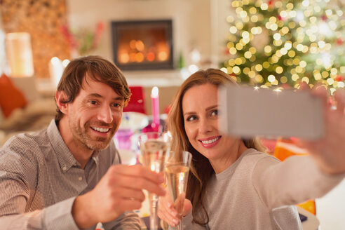 Lächelndes Paar stößt mit Sektflöten an und macht ein Selfie am Weihnachtstisch - HOXF01896