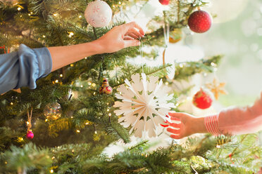 Mother and daughter hanging snowflake ornament on Christmas tree - HOXF01904