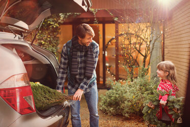 Vater und Tochter laden den Weihnachtsbaum aus dem Auto vor dem Haus aus - HOXF01906