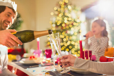 Husband pouring champagne for wife at Christmas dinner table - HOXF01908