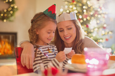 Mother and daughter wearing paper crowns at Christmas dinner table - HOXF01909