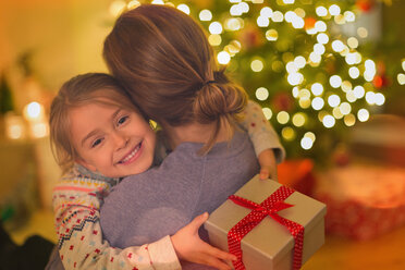 Lächelnde Tochter mit Weihnachtsgeschenk, die ihre Mutter umarmt - HOXF01922