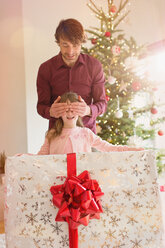 Vater verdeckt die Augen seiner Tochter, die ein großes Weihnachtsgeschenk hält - HOXF01928