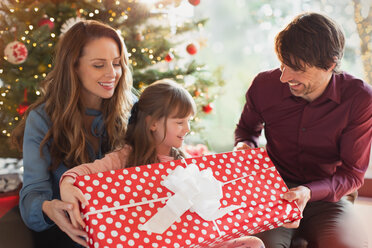 Eltern schenken ihrer Tochter ein großes Weihnachtsgeschenk vor dem Weihnachtsbaum - HOXF01936