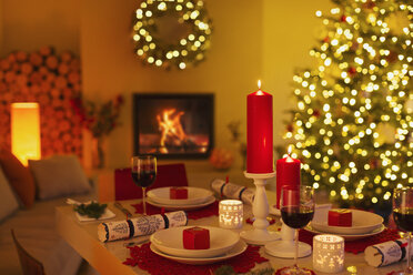 Stimmungsvolle Kerzen und Weihnachtsgebäck auf dem Esstisch im Wohnzimmer mit Kamin und Weihnachtsbaum - HOXF01938