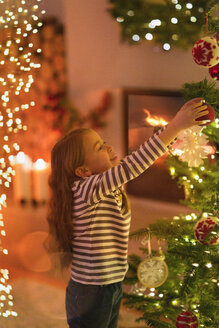 Mädchen hängt Ornament an Weihnachtsbaum - HOXF01943