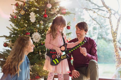 Eltern beobachten Tochter spielen Spielzeug Gitarre Weihnachtsgeschenk vor dem Weihnachtsbaum, lizenzfreies Stockfoto