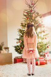 Girl in pink dress holding Christmas gift in front of Christmas tree - HOXF01954