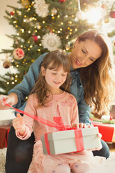 Mutter hilft Tochter beim Öffnen des Weihnachtsgeschenks - HOXF01963