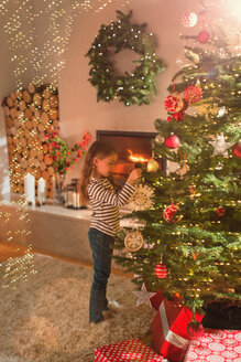 Mädchen hängt Schneeflocke Ornament auf Weihnachtsbaum im Wohnzimmer - HOXF01967