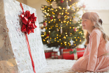 Mädchen lächelt in Erwartung eines großen Weihnachtsgeschenks am Weihnachtsbaum - HOXF01969