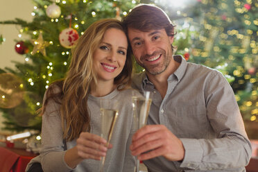Portrait lächelndes Paar stößt mit Sektflöten vor einem Weihnachtsbaum an - HOXF01976