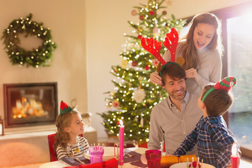 Familie mit Elfe und kostümiertem Rentiergeweih am weihnachtlichen Esstisch - HOXF01979