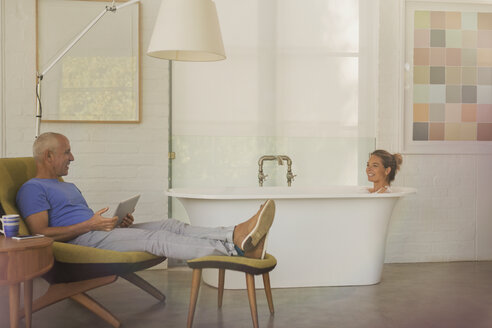 Ehemann mit digitalem Tablet entspannt sich, spricht mit Frau in der Badewanne in einem Luxushotelzimmer - HOXF02018