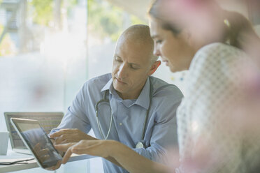 Männlicher Arzt zeigt einer Patientin in der Arztpraxis ein digitales Tablet - HOXF02025